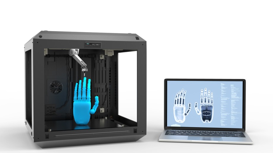 手がプリントされている3Dプリンターとノートパソコン